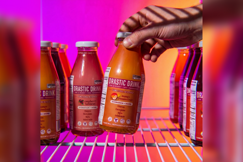 Bottle of Drastic Drink being held above a row of similar bottles on a colorful background 
